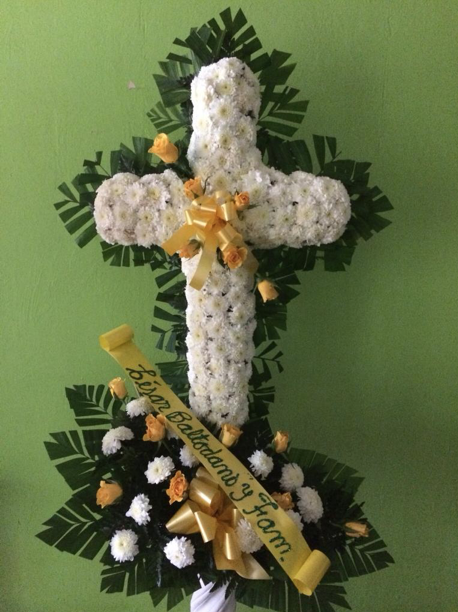 Una cruz hecha de flores blancas con un lazo amarillo.